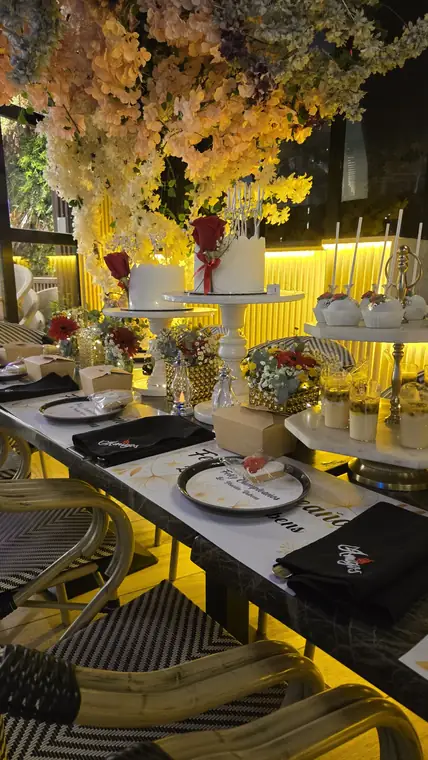 Mesa de cumpleaños bajo flores con servilletas bordadas con el logo de Amigos