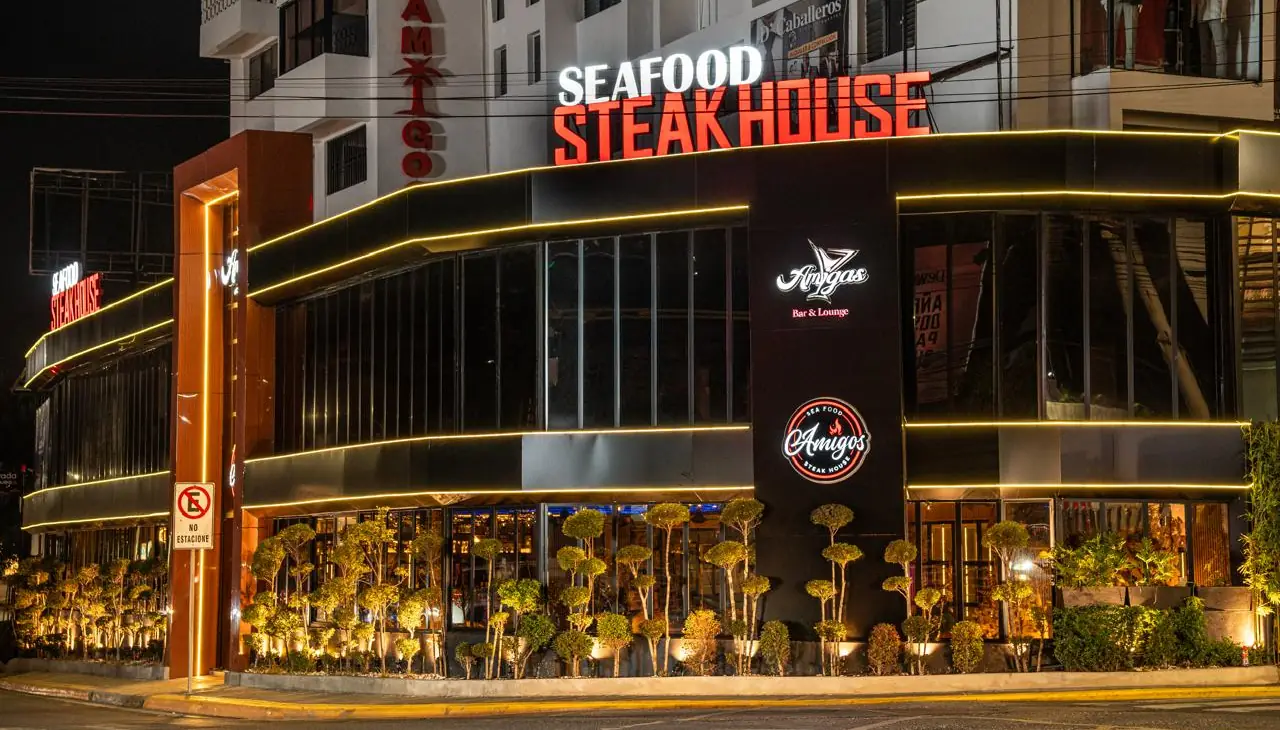 Fachada iluminada de Amigos Seafood & Steak House en la avenida Estrella Sadhalá, Santiago