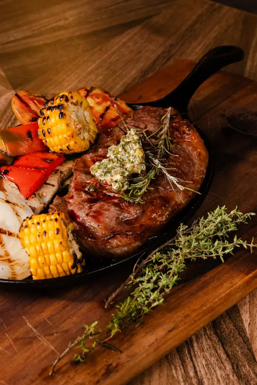 Ribeye en sartén de hierro con vegetales a la parrilla y mantequilla de hierbas